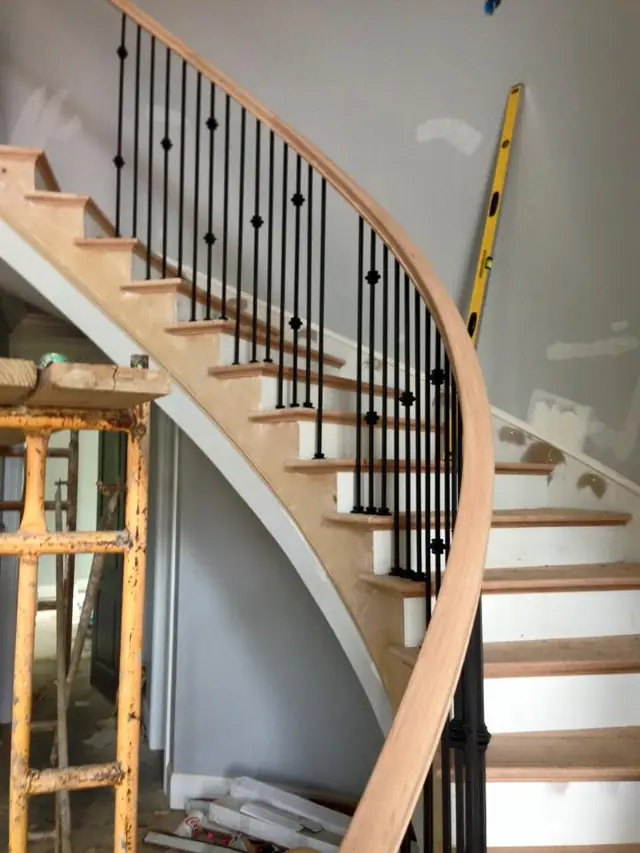 A curved staircase mid-install, iron balusters set and scaffold still up