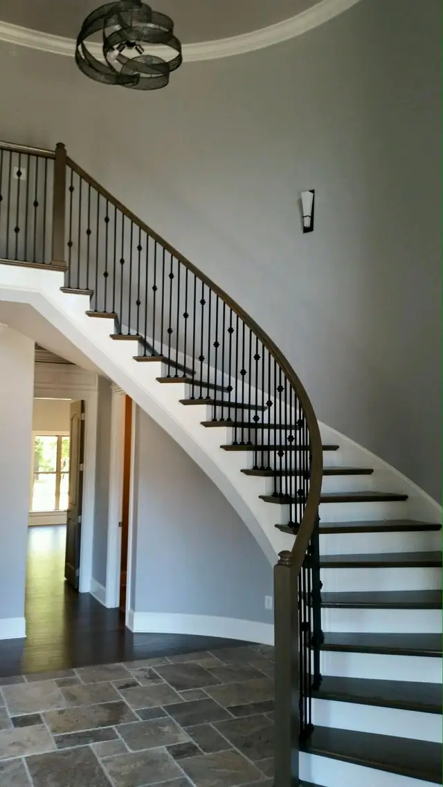 A finished curved staircase with dark treads, white risers and an iron-baluster rail