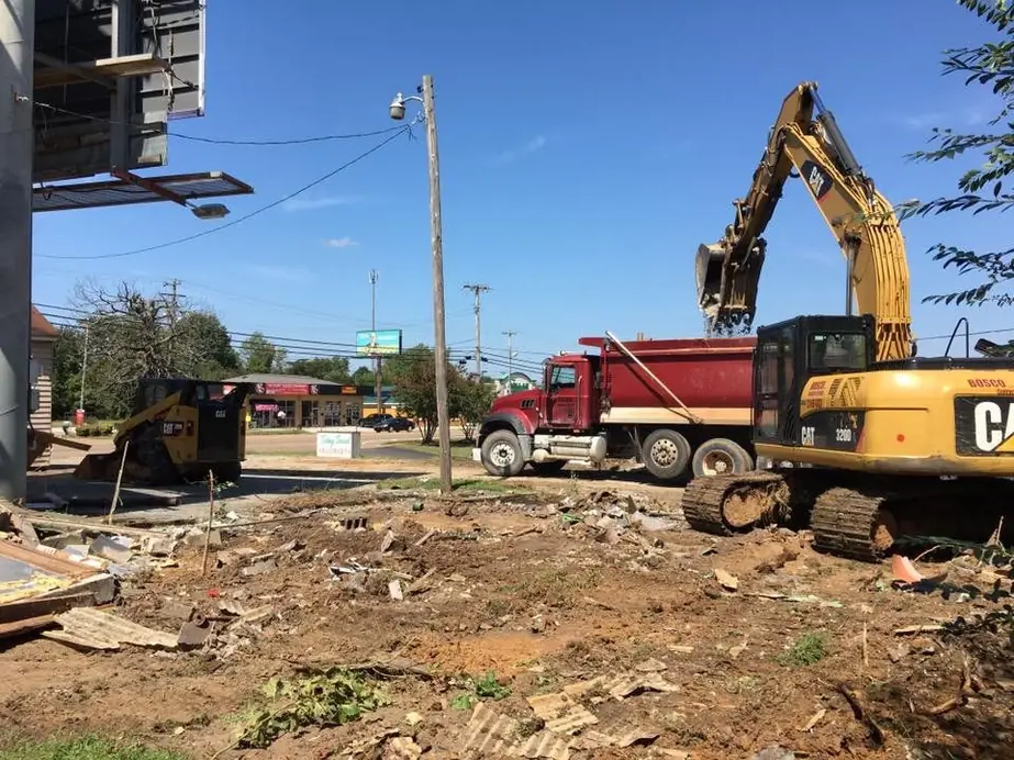 A CAT excavator and a red dump truck on a commercial lot after the building has come down