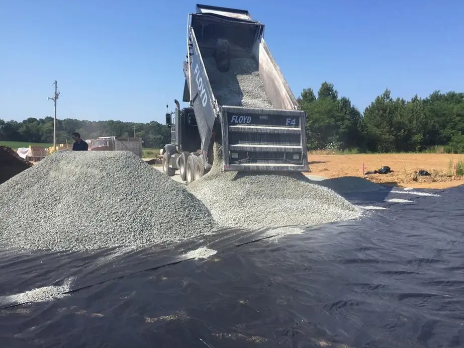 A dump truck tipping a load of crushed gravel onto black ground fabric